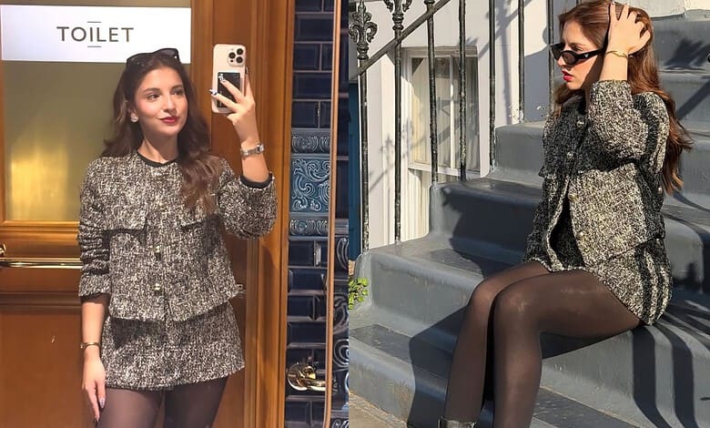 A woman taking a mirror selfie in a stylish mini skirt and blazer outfit, with a "TOILET" sign visible in.