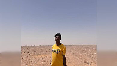 Young man standing in a vast, arid desert landscape under a clear blue sky.