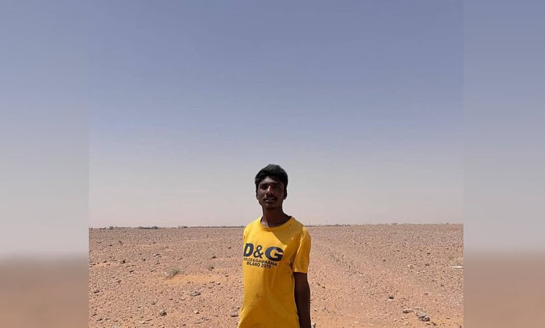 Young man standing in a vast, arid desert landscape under a clear blue sky.
