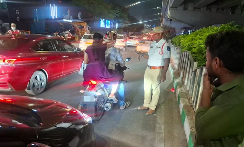 Traffic police stop vehicle on busy Hyderabad street at night.