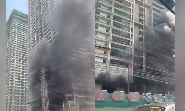 Fire incident at high-rise building with thick black smoke and flames, urban area with construction and v.
