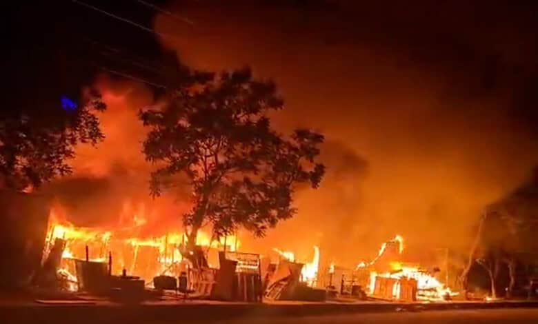 Fire outbreak at night with flames and smoke engulfing buildings and trees.