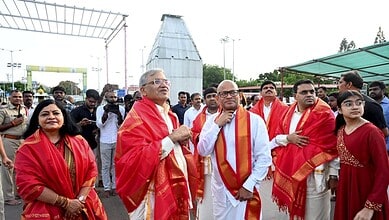 Celebration event with dignitaries and attendees wearing traditional red shawls at an outdoor gathering.