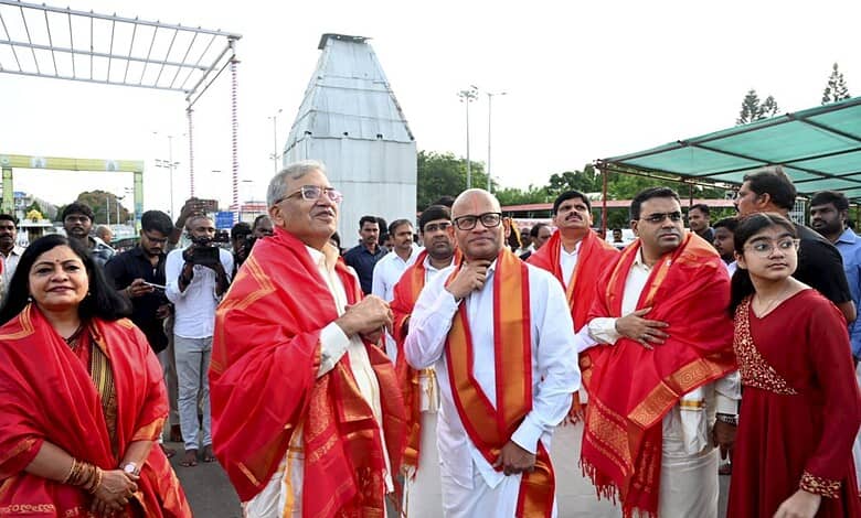 Celebration event with dignitaries and attendees wearing traditional red shawls at an outdoor gathering.