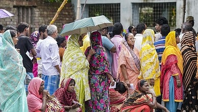 Crowd of voters, including women with umbrellas, at polling stations during Bengal repoll.