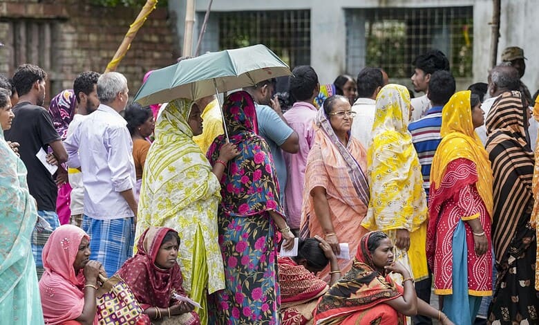 Crowd of voters, including women with umbrellas, at polling stations during Bengal repoll.
