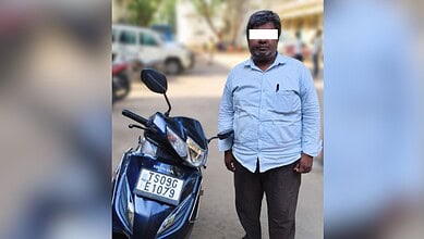 Man standing next to a scooter with a fake number plate in Hyderabad, police arresting suspect for using.