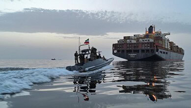 A small patrol boat with Indian flags sailing near a large cargo ship in open waters during cloudy weathe.