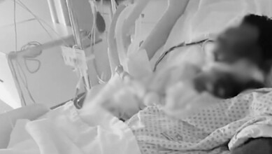 Patient on ventilator in hospital ICU with medical staff attending.