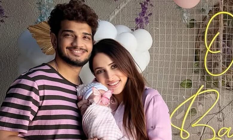 A newborn girl with her parents celebrating at a festive event, smiling and dressed in pink, with decorat.