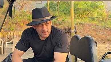 Salman Khan wearing a black hat and t-shirt outdoors, with greenery in the background.
