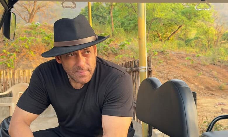 Salman Khan wearing a black hat and t-shirt outdoors, with greenery in the background.