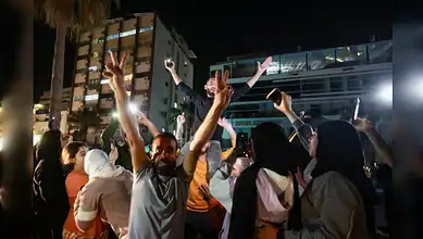 Residents celebrate in the coastal city of Sidon at night, raising victory signs and mobile phones in the street.