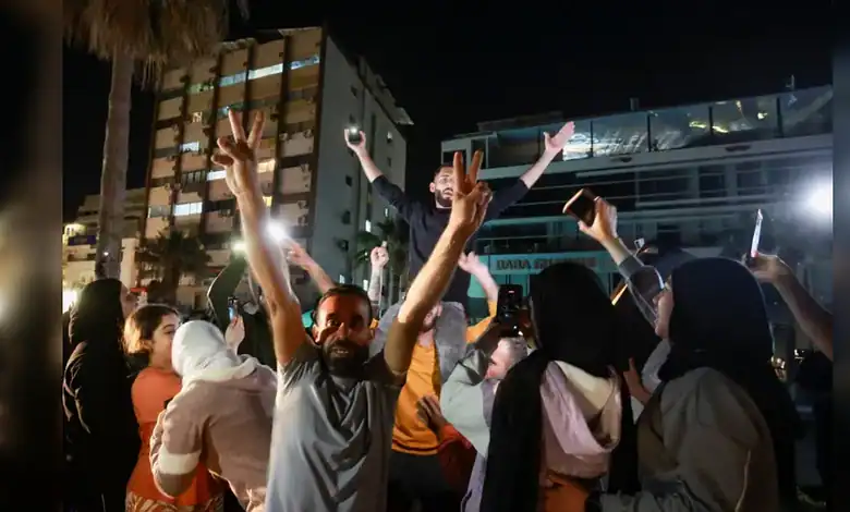 Residents celebrate in the coastal city of Sidon at night, raising victory signs and mobile phones in the street.