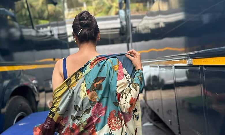 A woman in a colorful saree walking near parked vehicles in an urban setting.