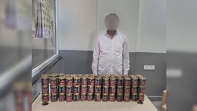 A person standing behind a table with numerous cans of food, likely for donation or distribution purposes.