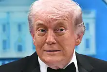 Donald Trump at a press event, delivering a speech in a professional environment.