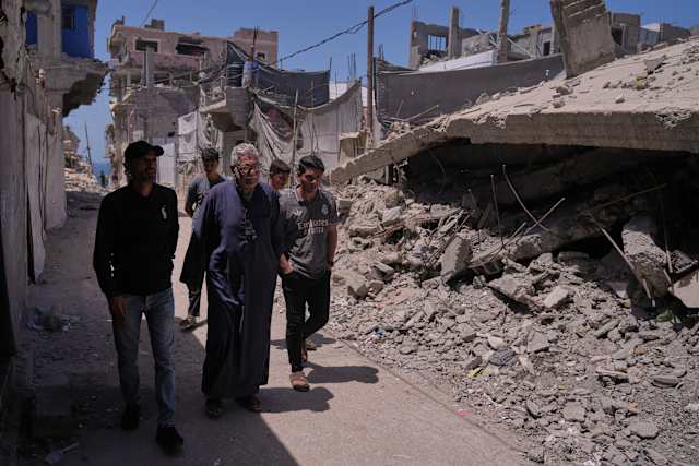 Palestinian Nakba survivor Yusuf Abu Hamam walks with family members past destroyed buildings in Gaza’s Shati refugee camp.
